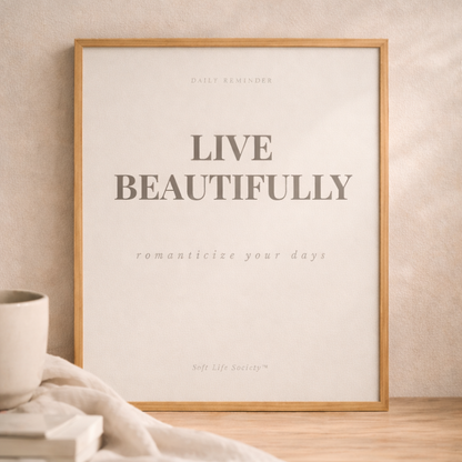 Framed print with 'Live Beautifully' text on a wall with a cup and blanket in the foreground.