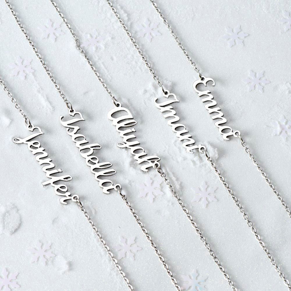 Assorted silver and gold personalized name necklaces arranged on soft white fabric for a flat-lay display.