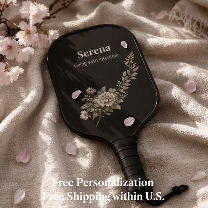 Black paddle with floral design and 'Serena' branding on a beige fabric background with cherry blossoms.