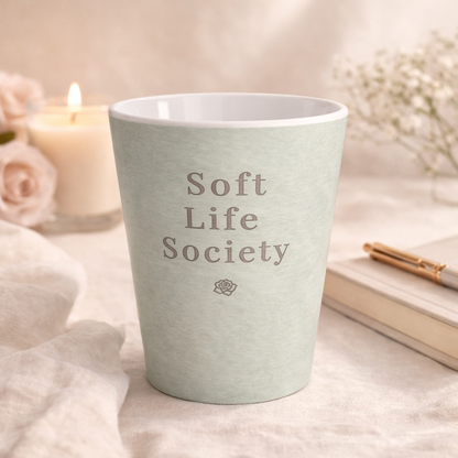 Light green mug with 'Soft Life Society' text on a soft background with candles and flowers.