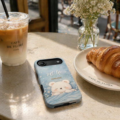 Soft blue “Soft Life Activated” phone case on café table with iced coffee and croissant, everyday aesthetic lifestyle