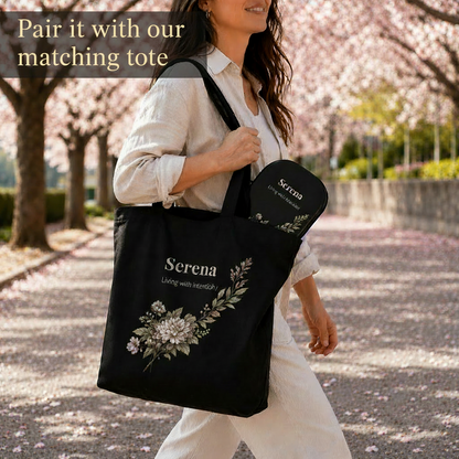 Woman holding a black tote bag with floral design and 'Serena' branding in a cherry blossom garden.