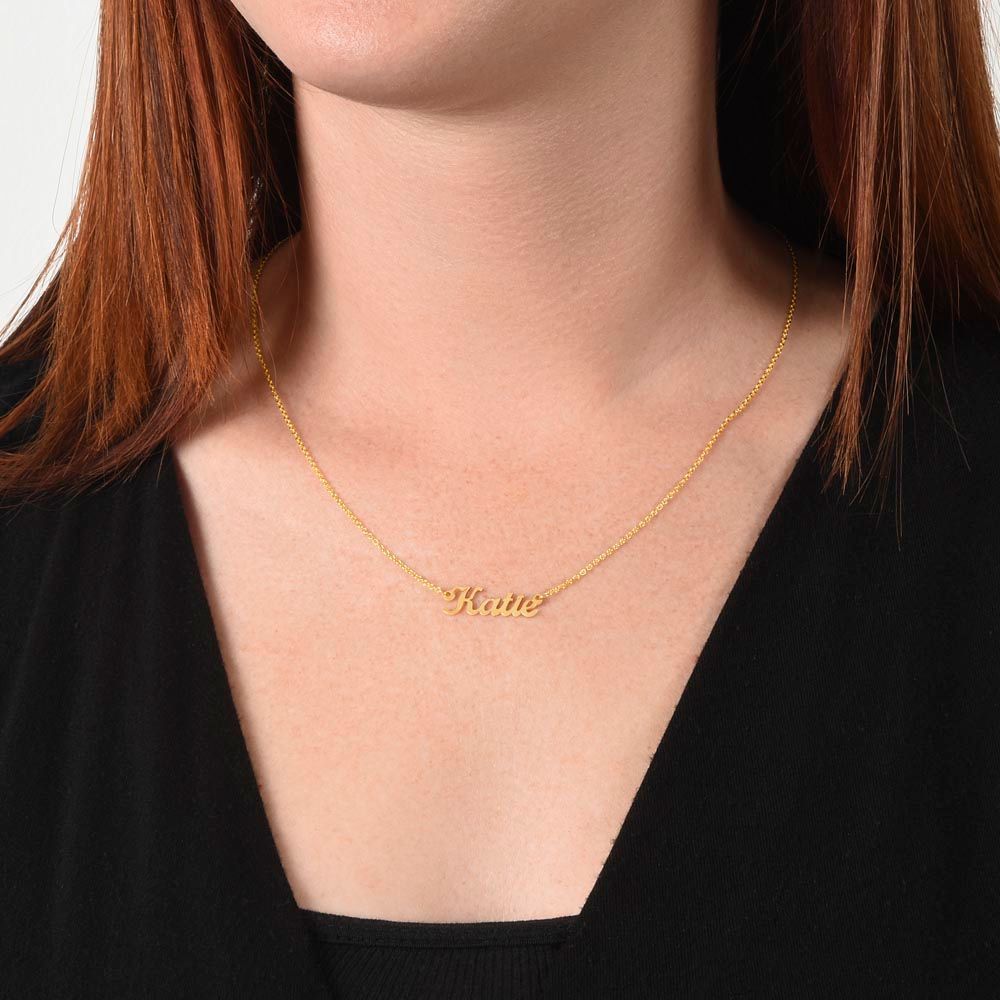 Woman wearing a gold personalized name necklace, styled with a minimal neckline.