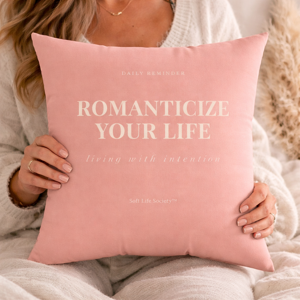 Person holding a pink pillow with text 'Romanticize Your Life' and 'Daily Reminder' on it.