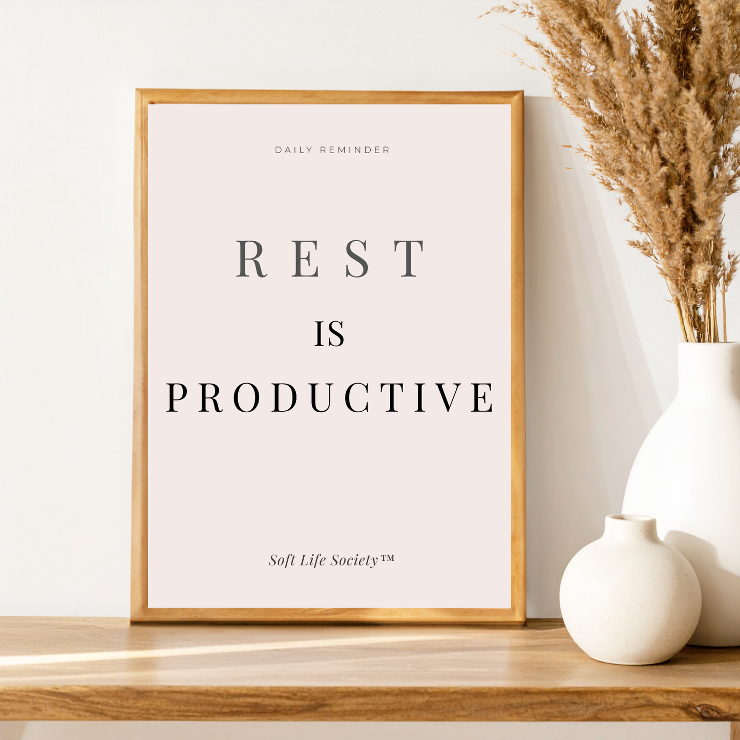 Framed print with 'Rest is Productive' text on a wooden shelf with decorative vases.