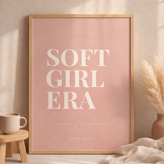 Framed poster with 'SOFT GIRL ERA' text on a pink background, placed in a room with decor elements.