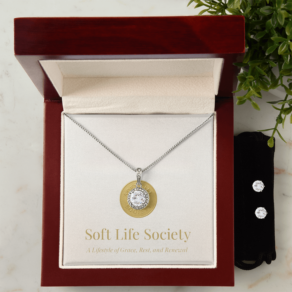 Silver crystal pendant necklace with round-cut stone, presented in a plush wooden Soft Life Society gift box alongside matching stud earrings.