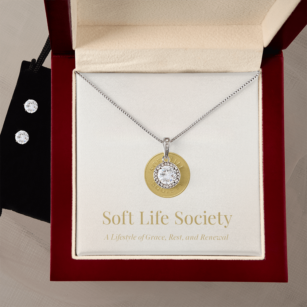 Women’s halo pendant necklace with sparkling round stone in cherry wood keepsake box, Soft Life Society branding and coordinating stud earrings.
