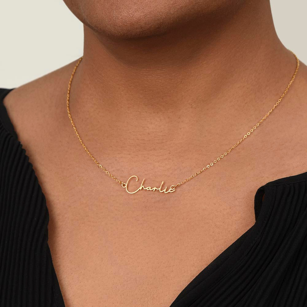 Person wearing the Soft Life Society Signature Style Name Necklace in 18K yellow gold with “Charlie” script pendant, styled with a black pleated top.