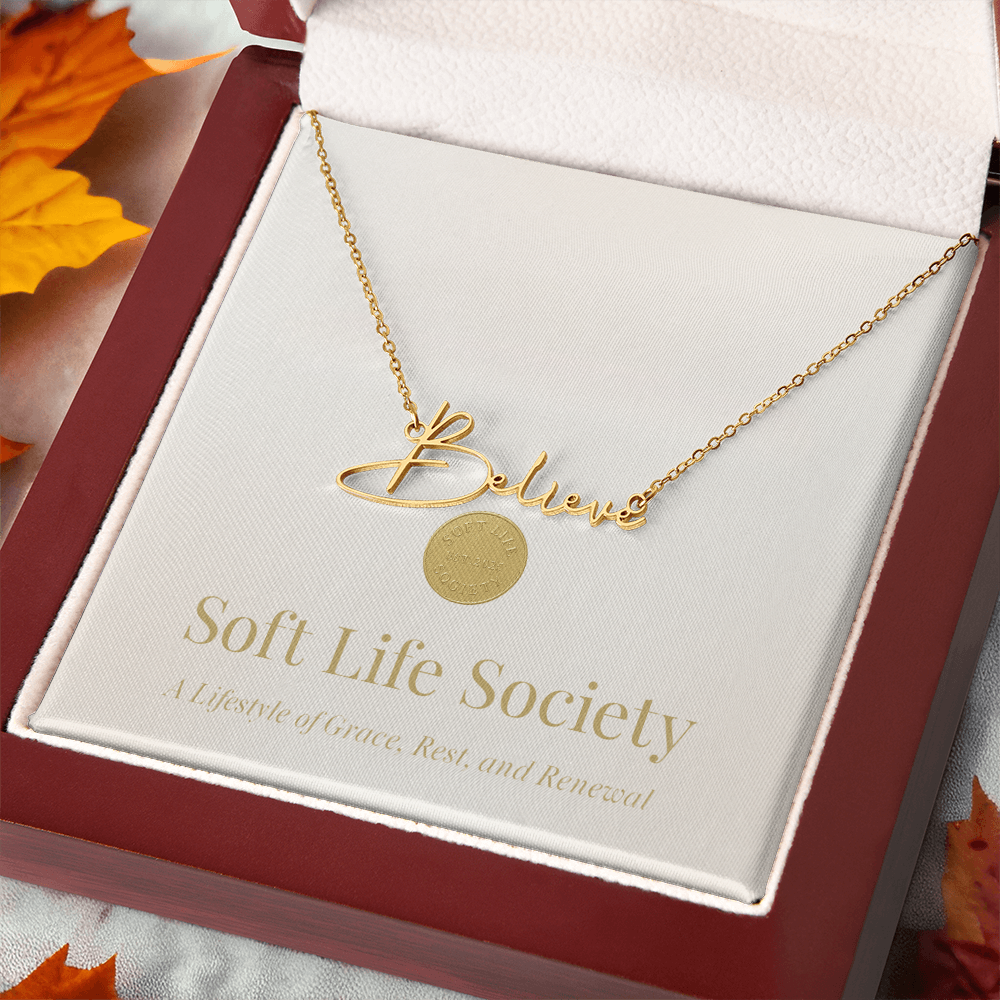 Soft Life Society Signature Style Name Necklace in 18K yellow gold with “Believe” script pendant displayed in a mahogany luxury gift box on a soft autumn background.