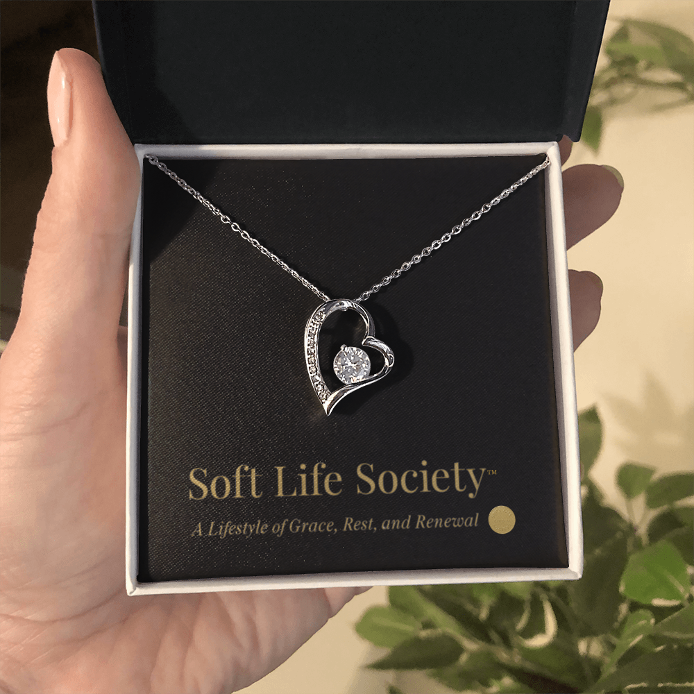 Close-up of silver Forever Love Necklace held in hand with Soft Life Society™ card.