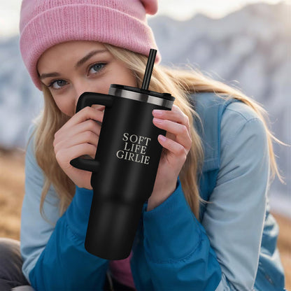 Woman holding a black Soft Life Girlie™ 40oz insulated tumbler with handle and straw while sitting outdoors in cool weather.