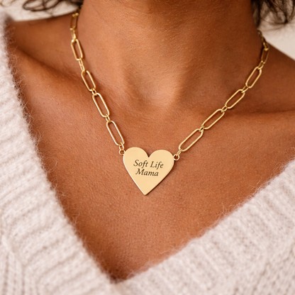 Gold paperclip chain necklace with a heart-shaped 'Soft Life Mama' pendant on a person wearing a white sweater.
