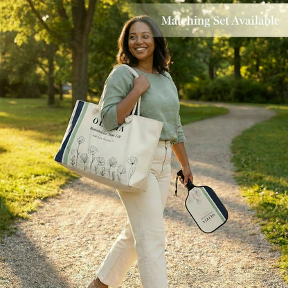 Woman walking outdoors holding a tote bag and a small bag, with trees and grass in the background.