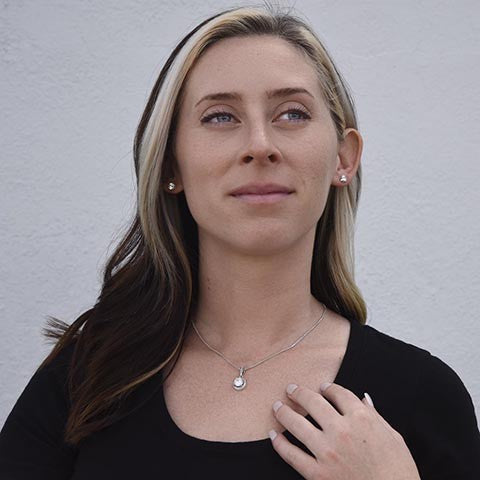 Woman wearing a silver halo pendant necklace and matching stud earrings from Soft Life Society.