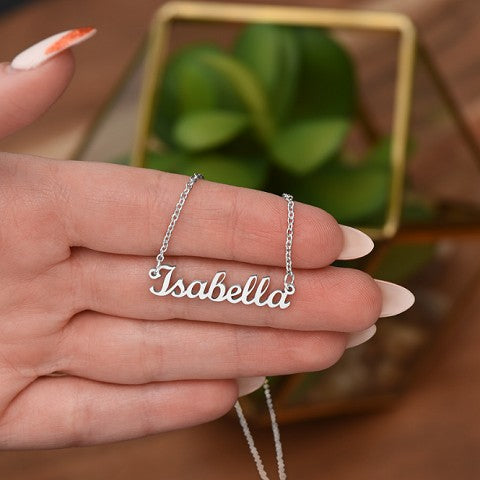 Silver 'Isabella' necklace held by a hand with a blurred green plant in the background