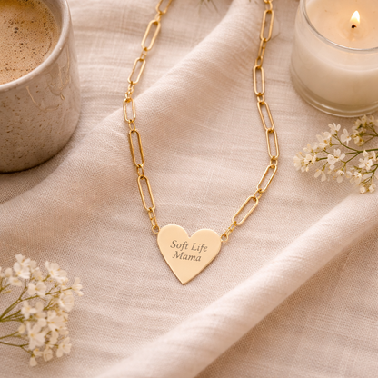 Gold necklace with a heart-shaped pendant on a beige fabric background with a cup of coffee and candle.