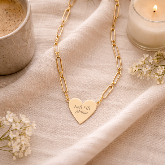 Gold necklace with a heart-shaped pendant on a beige fabric background with a cup of coffee and candle.