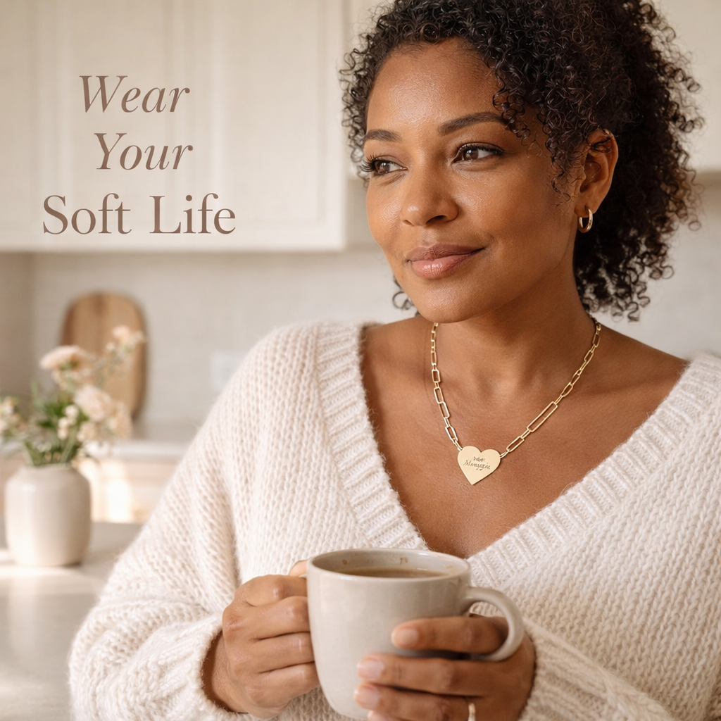 Woman holding a mug with 'Wear Your Soft Life' text in a cozy indoor setting wearing 'Soft Life Mama' paperclip necklace.