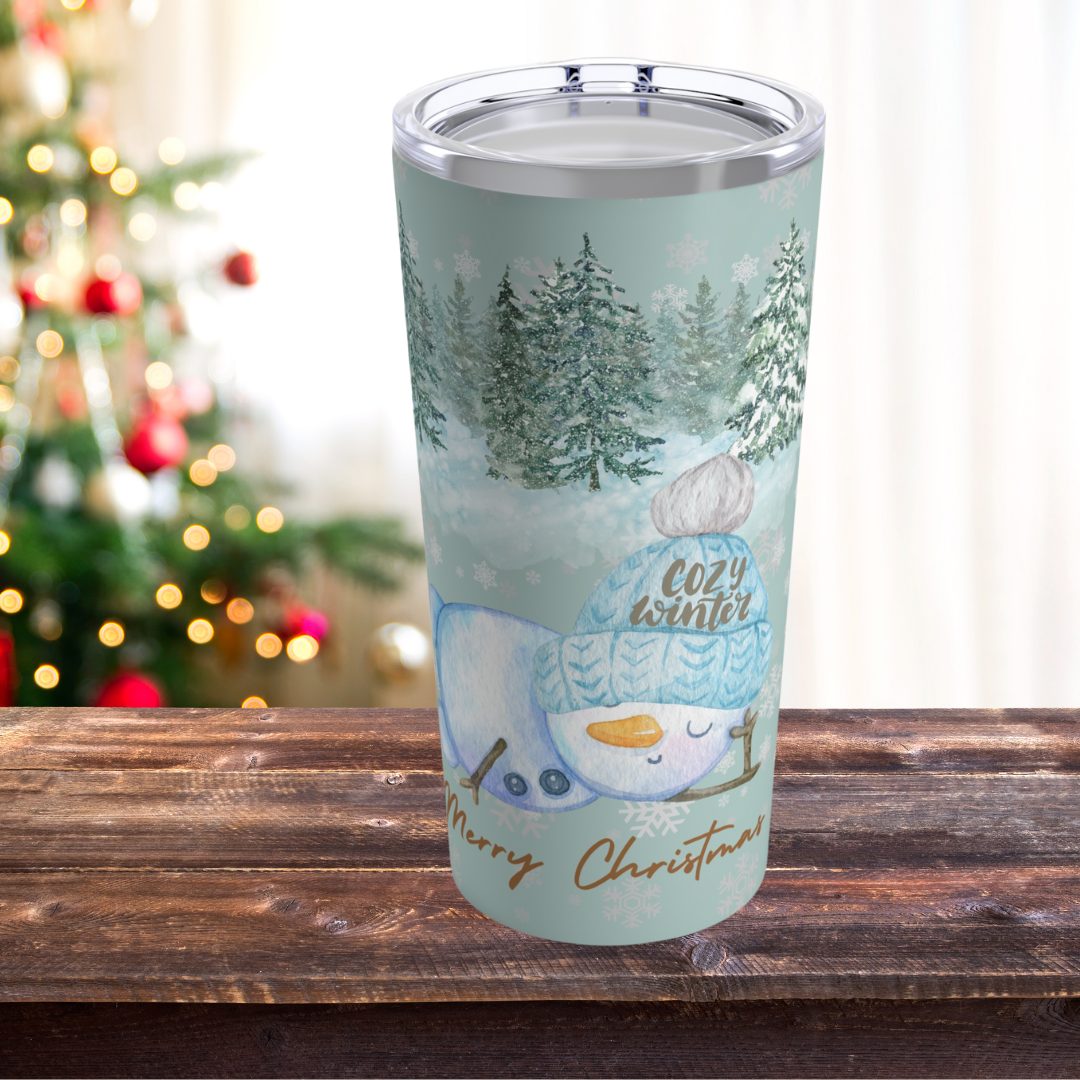 20oz insulated Christmas tumbler featuring a cute snowman in a winter forest scene, with 'Cozy Winter' text. Perfect for holiday season warmth and cheer.